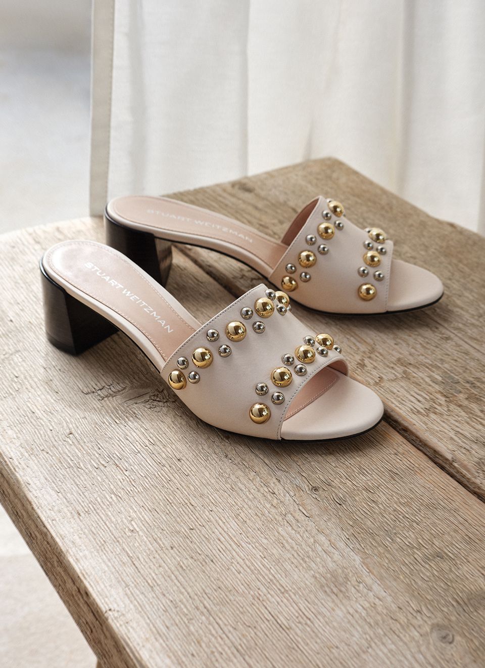 The Perry Slide Sandal 50 in linen leather with mixed-metal dome studs and maroon block heel, on a wooden surface 
